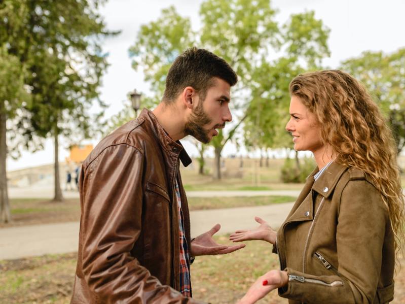 A man and woman arguing outside near a park