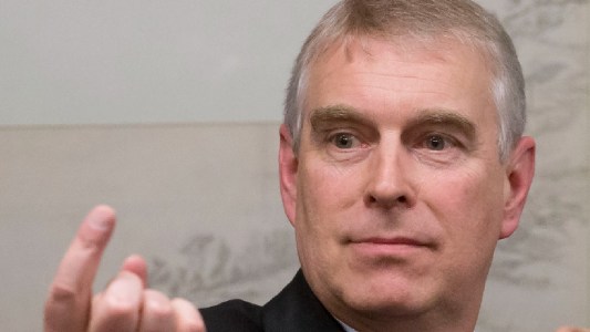 Prince Andrew wears a black suit and makes a hand gesture during a public appearance