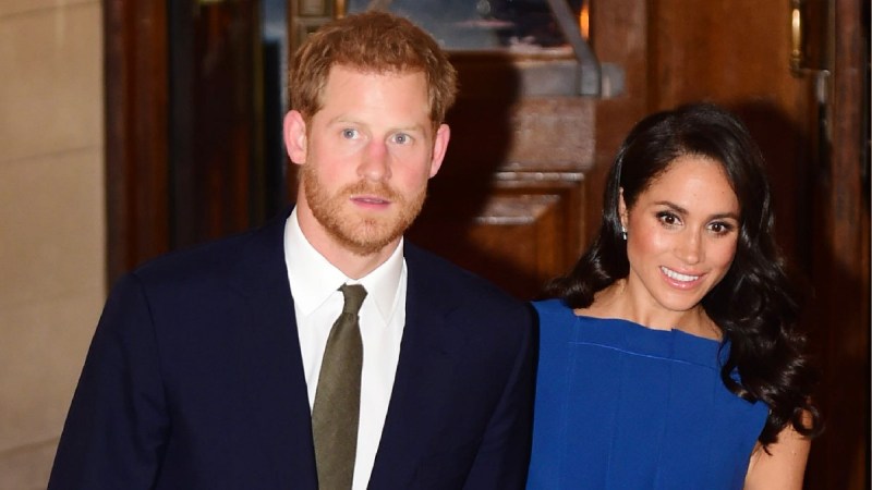 Prince Harry, in a dark suit, walks with wife Meghan Markle, in a blue dress, in a London concert hall