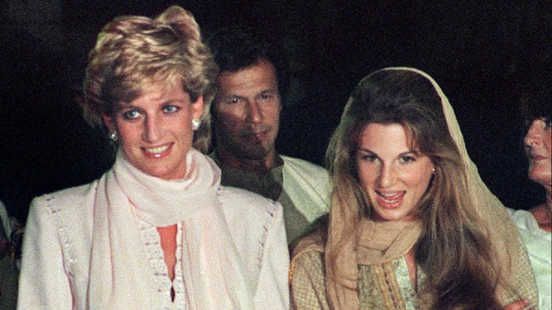 Princess Diana, in white, walks with friend Jemima Khan, in a tan headscarf, outdoors