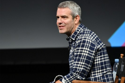 Andy Cohen in a plaid shirt, sitting on a stage