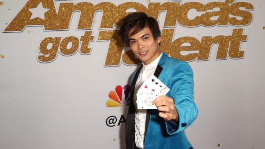 Shin Lim wears a blue blazer and holds up playing cards on the red carpet
