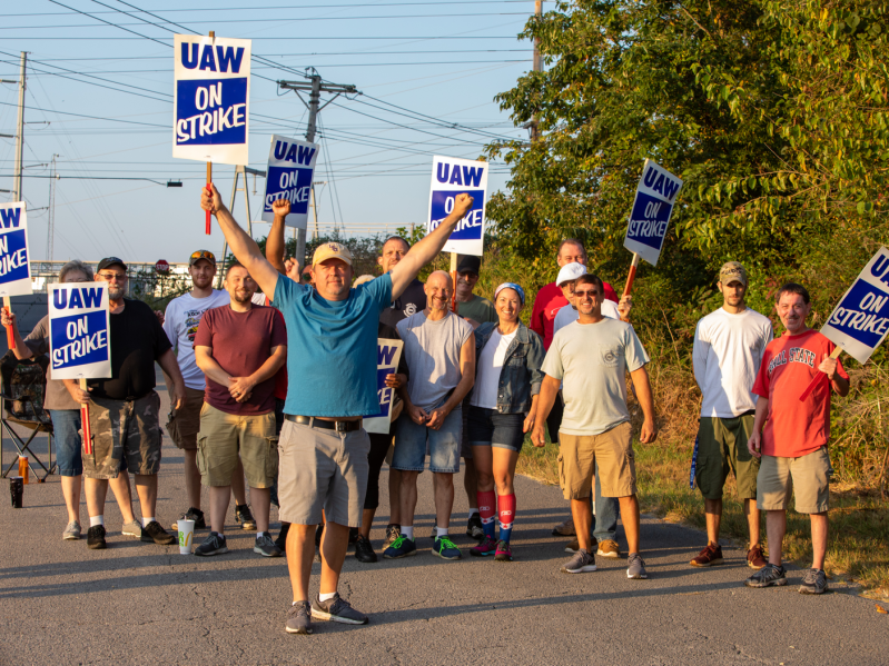 A group of workers on strike walk down a street while holding signs