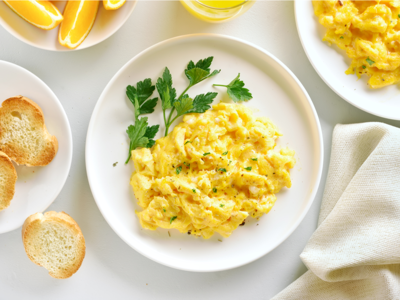 Scrambled Eggs on white plate surrounding by toast and other breakfast foods