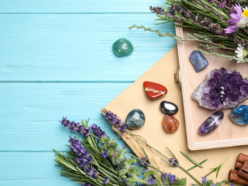 Gemstones and healing herbs on light blue wooden table, flat lay.