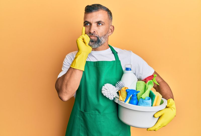 Confused man holding cleaning supplies.