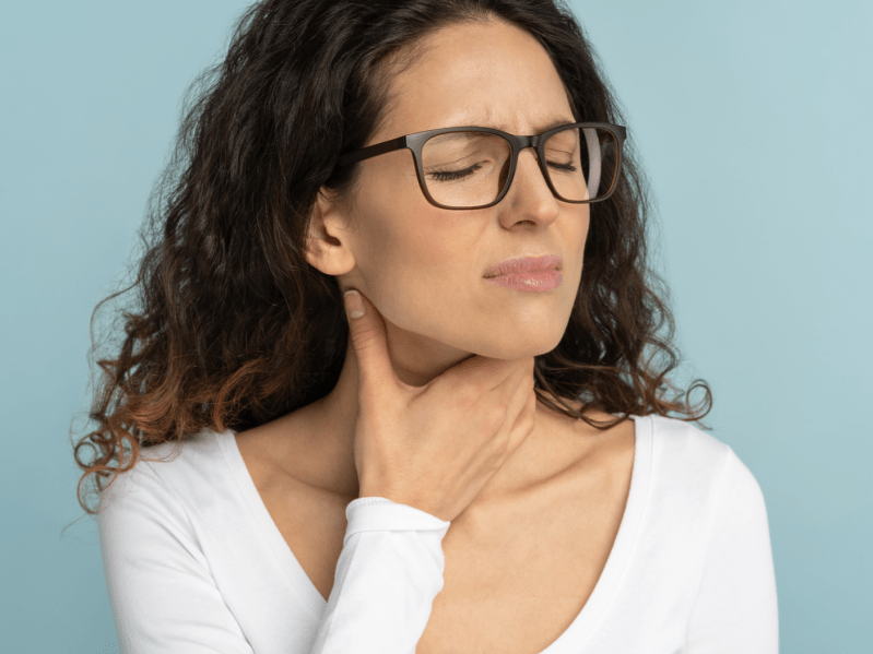 Woman with glasses holding her throat on light blue background