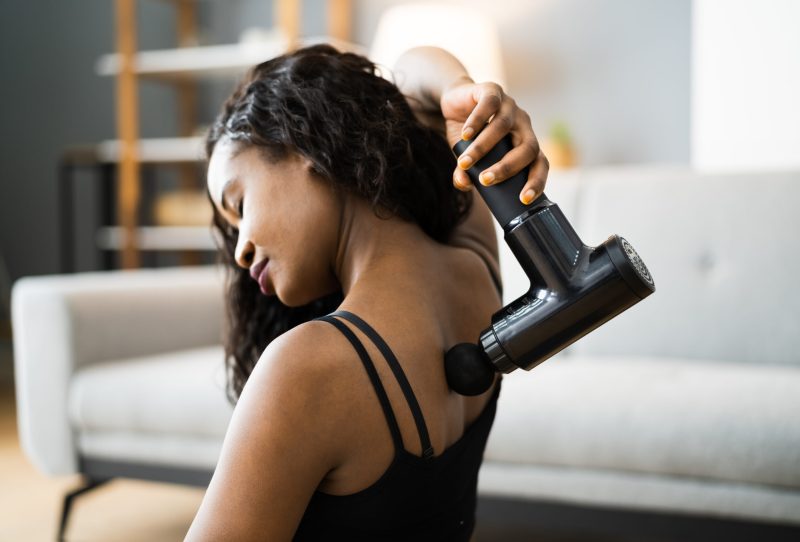 Woman using a massage gun to relieve back pain.