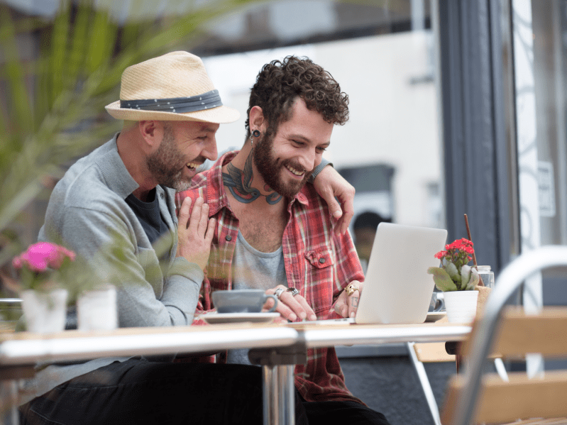 Gay couple sat sharing laptop outside a cafe