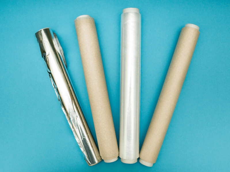 Four rolls of wax paper, parchment paper, and aluminum foil on a blue background