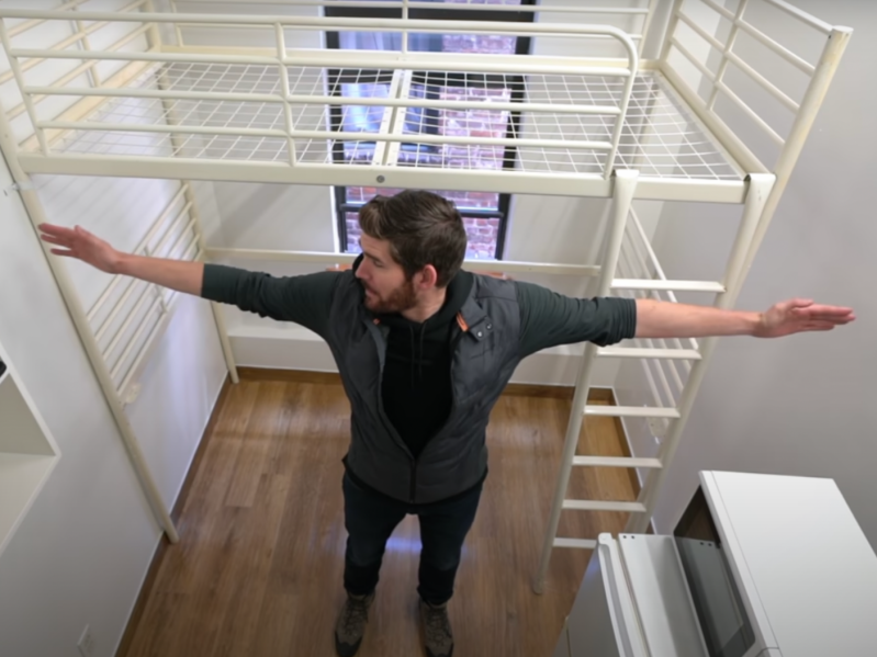 Erik Conover standing in the center of a micro-apartment and stretching his arms out to touch the walls