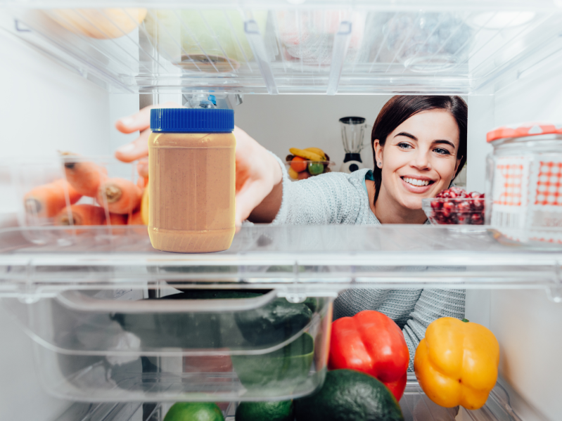 Woman reaching into a refrigerator to grab peanut butter.
