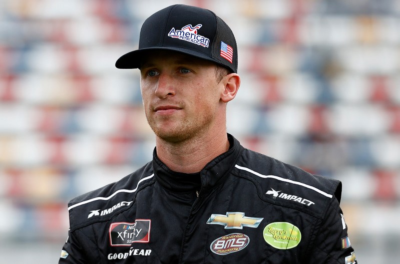 NASCAR driver Brandon Brown in his race suit and a baseball hat.