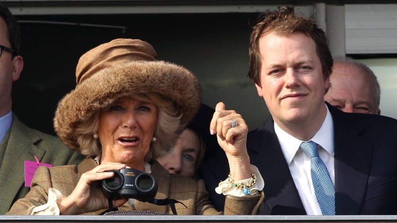 Camilla Parker Bowles, in a brown coat and hat, stands with her son Tom, in a dark suit