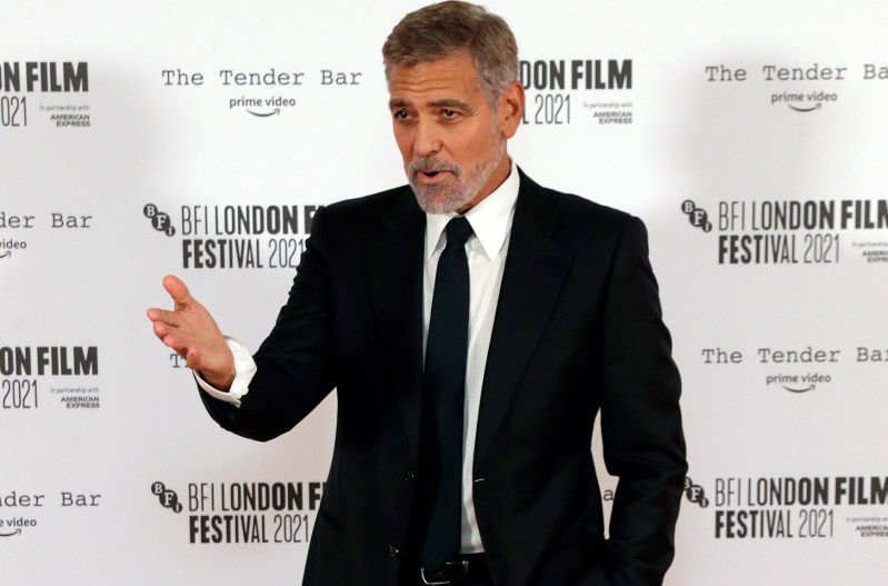 George Clooney in a dark suit, motioning with his right hand,