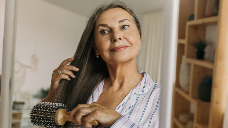 An older woman brushing her long brown hair in the mirror
