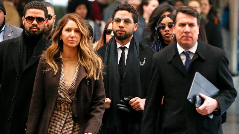Jussie Smollett, in a dark suit and coat, walks amid a crowd on his way to the courtroom