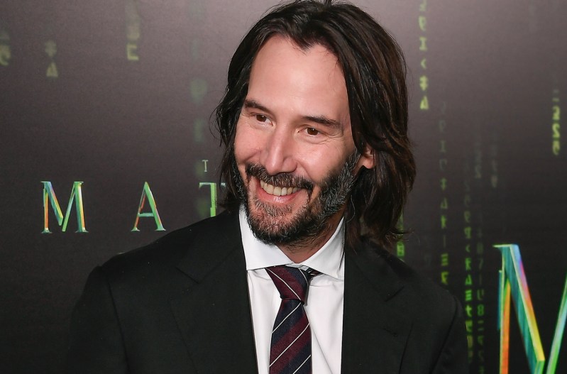Keanu reeves smiling in a dark suit at the latest Matrix Premiere