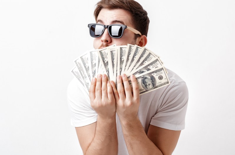A man wearing sunglasses fans out 100 dollar bills
