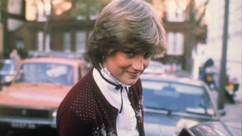 Princess Diana smiles demurely at the camera while walking outdoors in London
