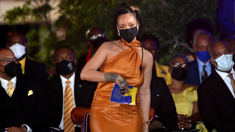 Rihanna wears an orange dress and holds a program in Barbados