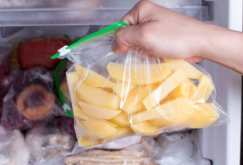 Bag of sliced potatoes being placed in the freezer.