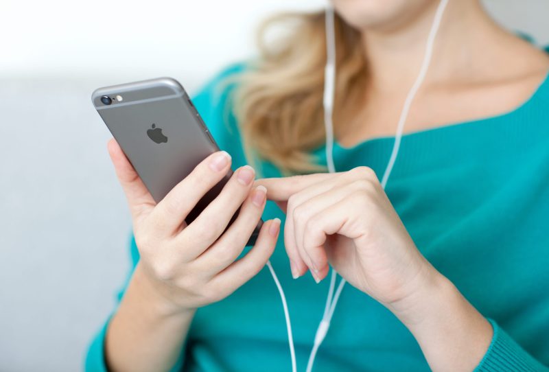 Woman holding an iPhone and wearing earbuds.