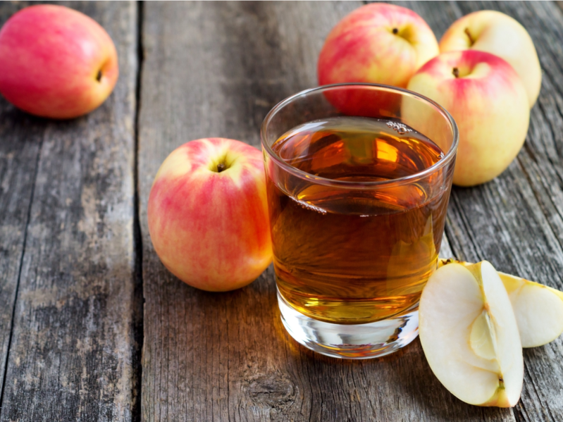Apple juice in a glass and apples on wooden background