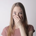 Young amazed woman in casual wear covering mouth while keeping secret