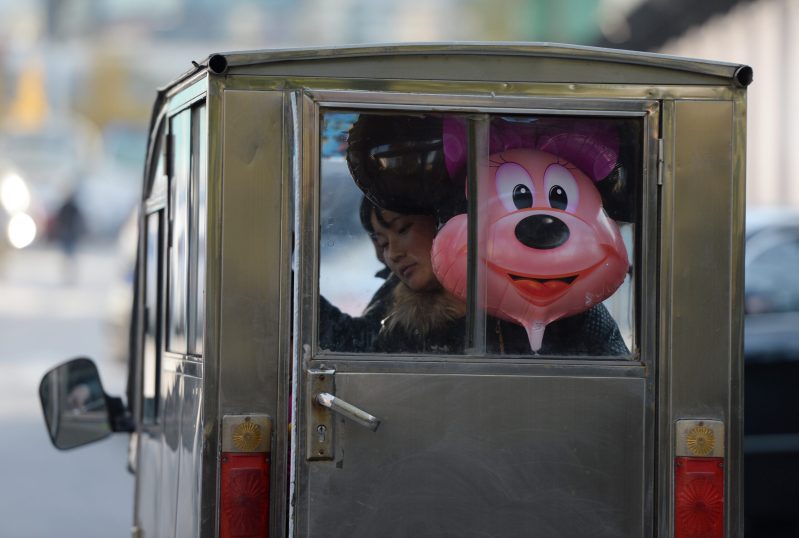 A creey photo of a Minnie Mouse Balloon looking out of the back of a car.