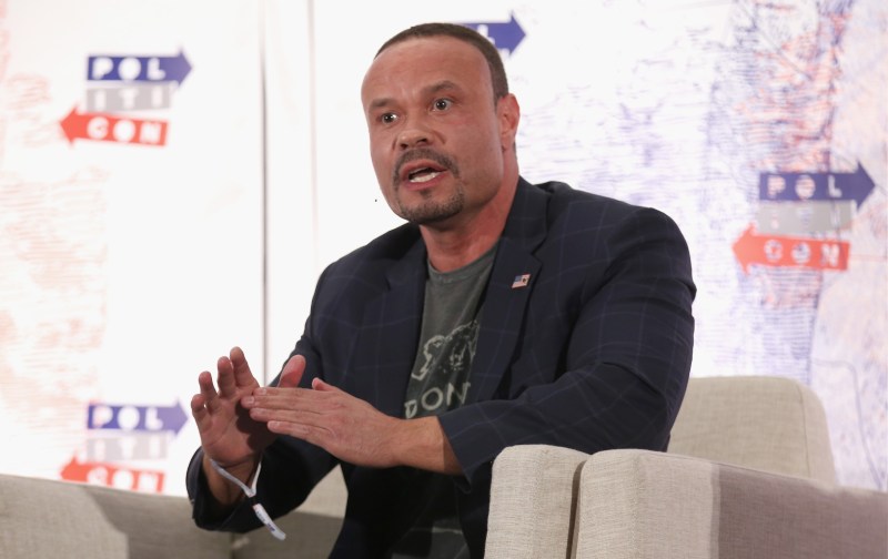 Dan Bongino wears a dark suit jacket as he makes remarks onstage