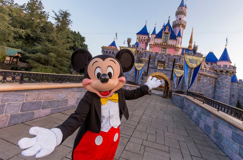 Mickey Mouse pointing towards Sleeping Beauty's Castle at Disneyland in California