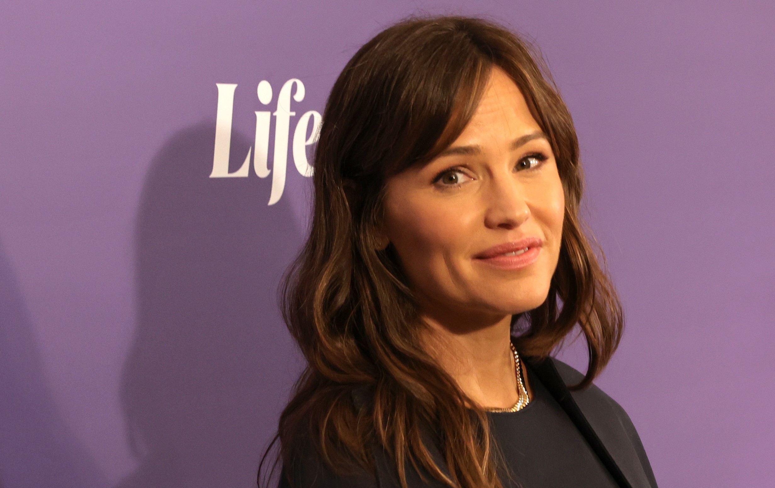 Jennifer Garner wears a black dress against a purple background on the red carpet