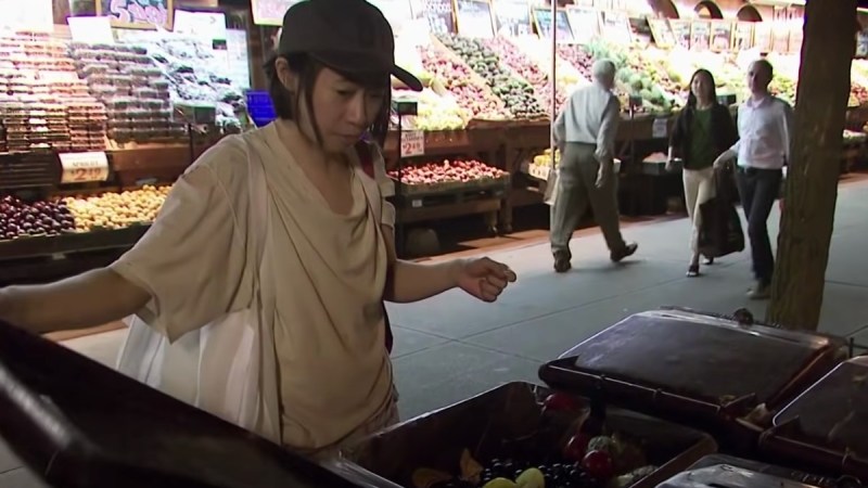 Kate Hashimoto, wearing a white top, digs through a garbage bin of fresh fruit in New York City