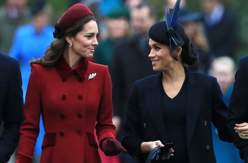 Kate Middleton in red, walking and talking to Meghan Markle in black