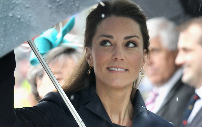 Kate Middleton wears a black jacket and holds an umbrella as she participates in a royal event