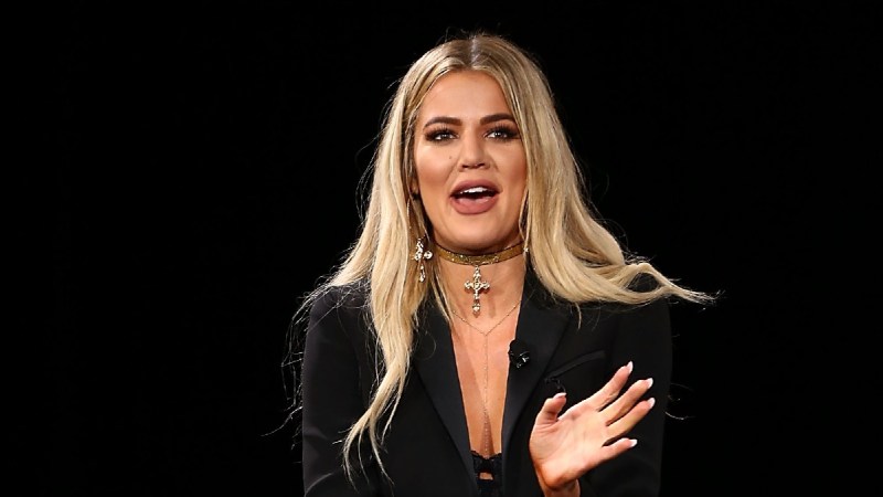 Khloe Kardashian wears a black pant suit on stage as she makes comments
