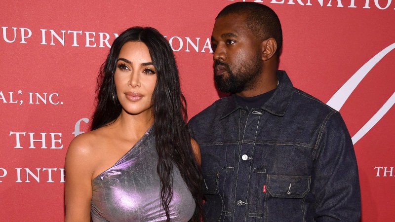 Kim Kardashian and Kanye West stand together in front of a red background