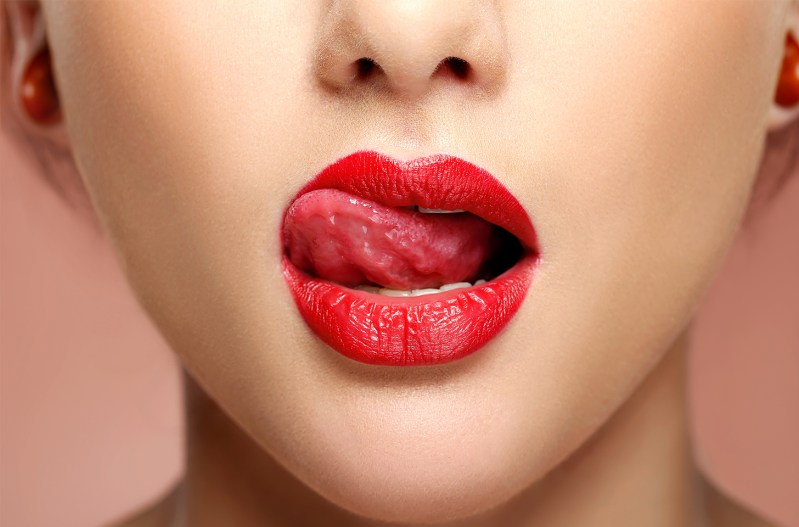 A woman licking her lips with red lipstick on