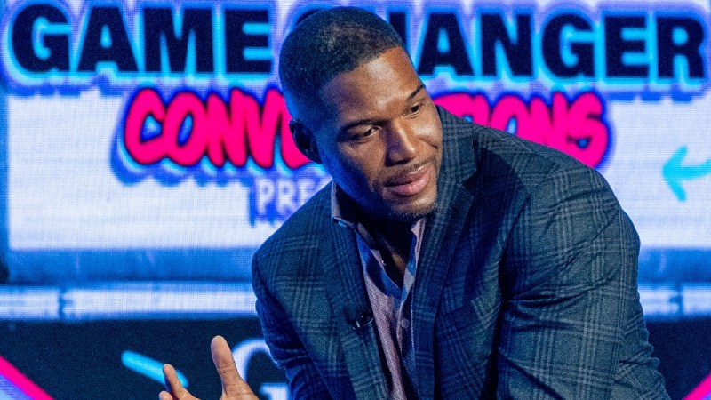 Michael Strahan gestures with both hands while making remarks onstage