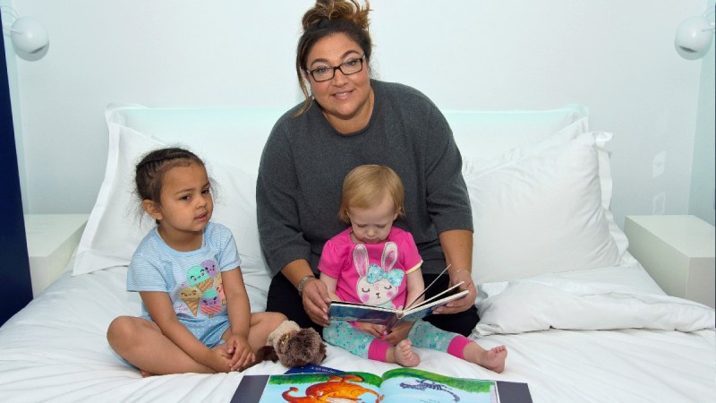 Jo Frost sits with two children on a bed while reading a book together