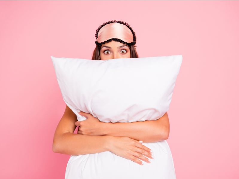 shocked lady wearing eye mask, hugging pillow, hiding. Isolated over pink pastel background