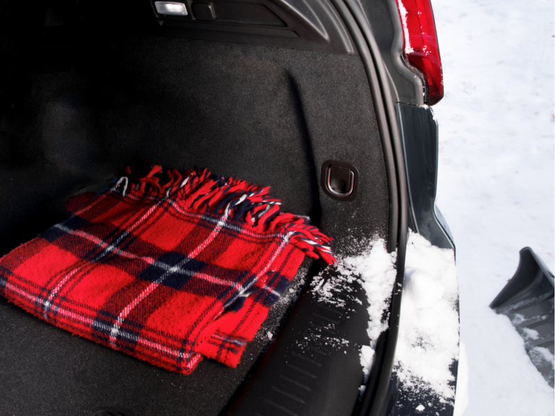 A red heated blanket sitting in the back of a car with snow on the ground