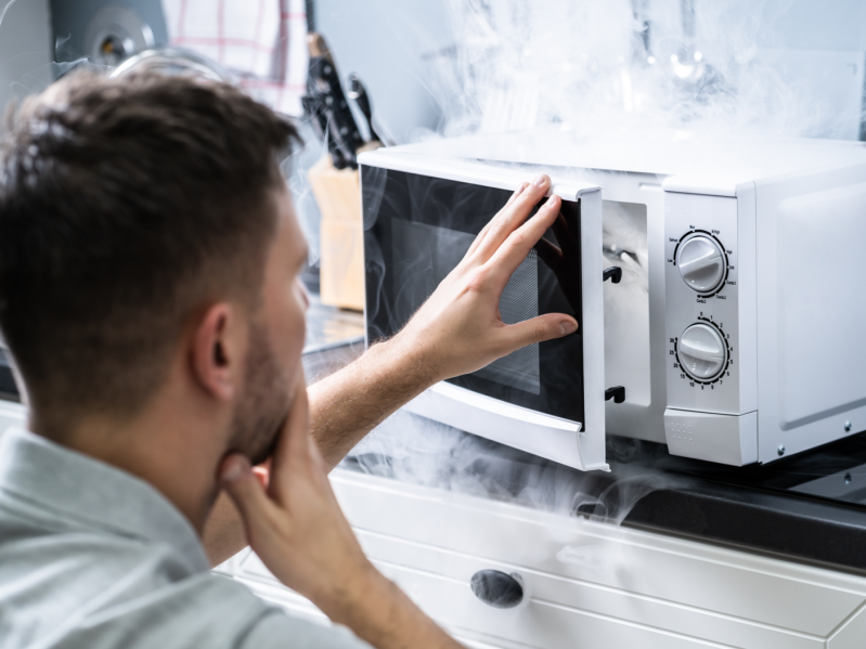 Young Man Spraying Fire Extinguisher On Microwave Oven In The Kitchen