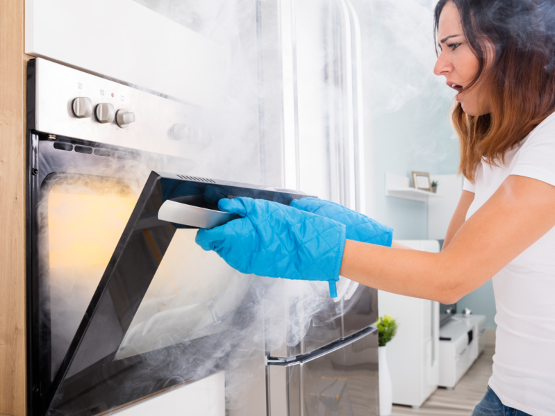 A woman opening an oven door and smoke pouring out