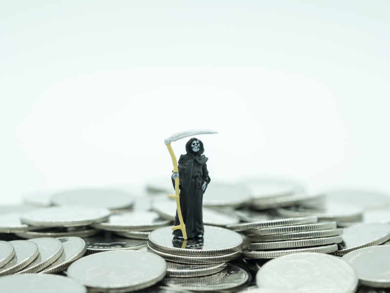 A small grim reaper toy standing on coins