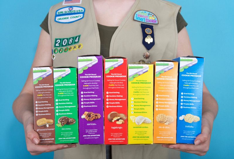 Girl scout holding several different boxes of Girl Scout cookies