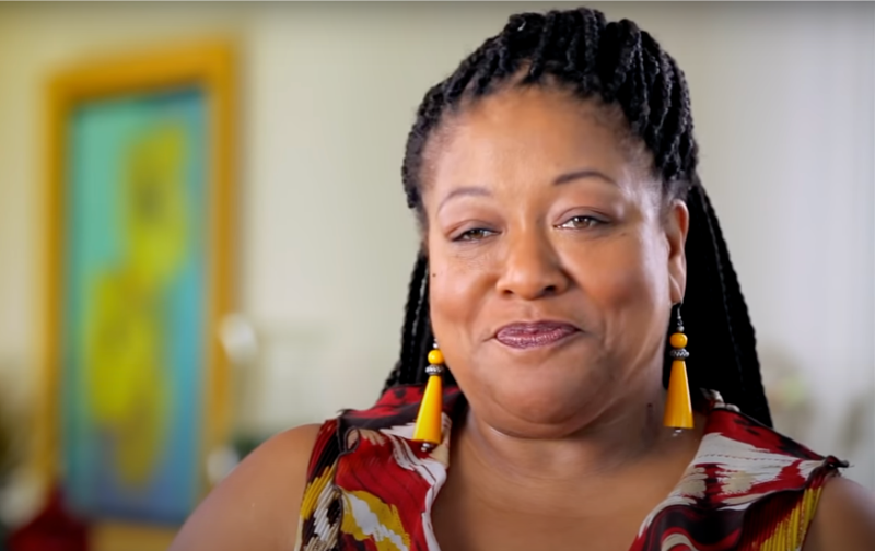 Diane Amos wears a red patterned shirt and sits at home for a video interview