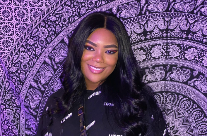 Riley Burruss smiling in front of a purple tapestry