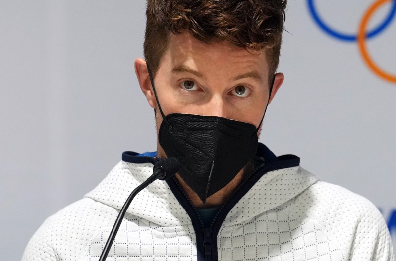 Shaun White looking skeptical, wearing a mask, at an Olympic press conference.